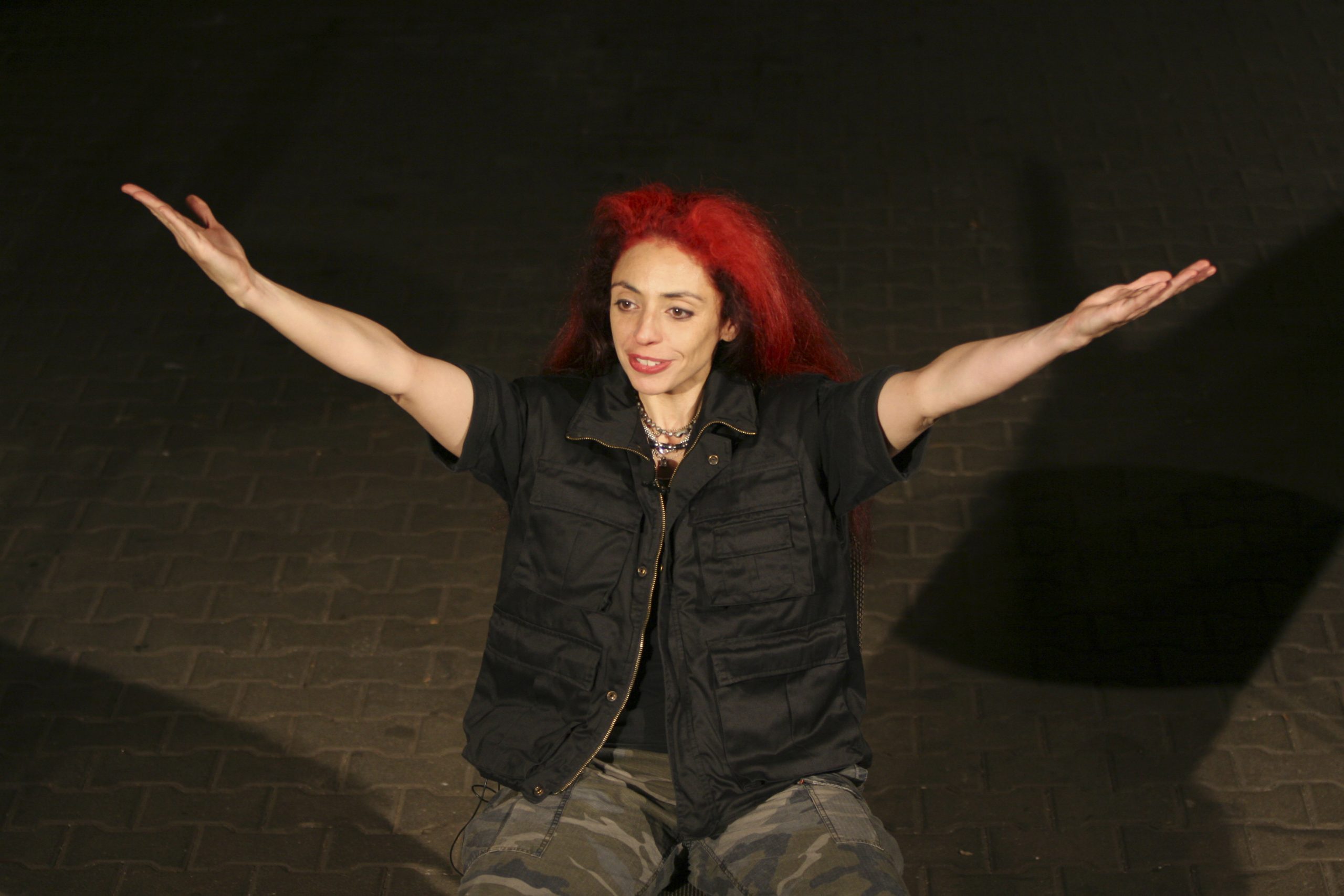 Isis führt Regie auf der Bühne sitzend mit nach oben ausgestreckten Armen Isis führt Regie auf der Bühne sitzend mit nach oben ausgestreckten Armen